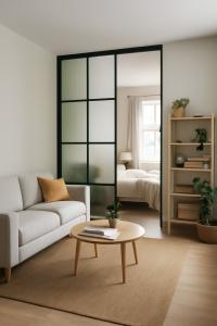 Modern living room with a sofa, wooden coffee table, and open view into a bedroom through a glass partition.