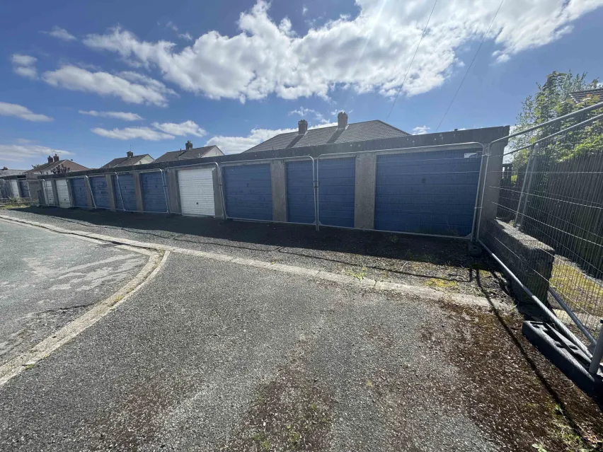 row of blue and white door single lock up garages sitting on a tarmac hardstanding.