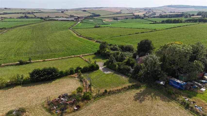 A mix of green fields and pasture land in a rural setting, with trees and bushes scattered around the boundary.