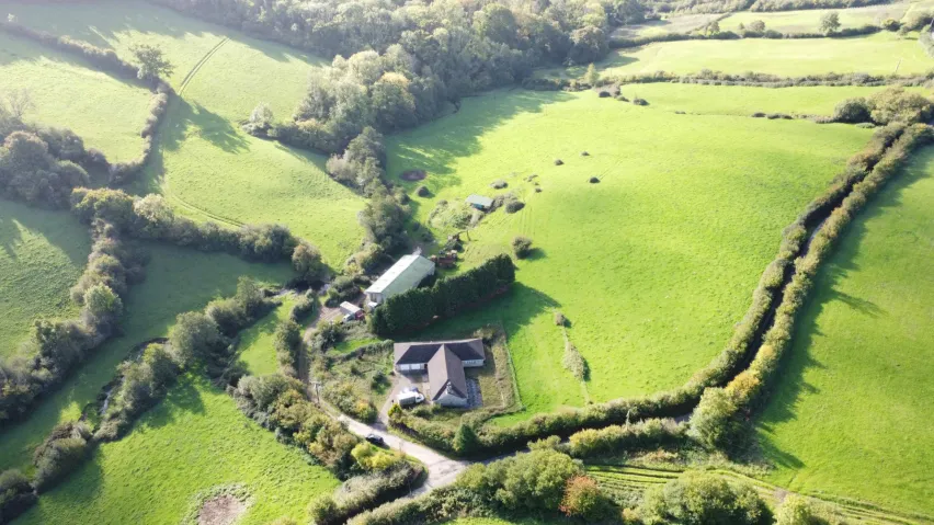 Aerial view of green fields with a bungalow and a barn in the middle.