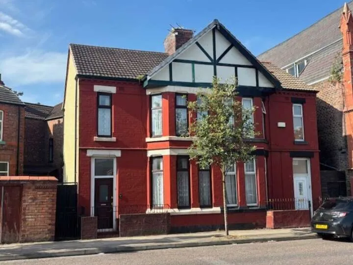 Red brick building comprising two semi detached houses with blue sky behind and a single tree in front of the building.