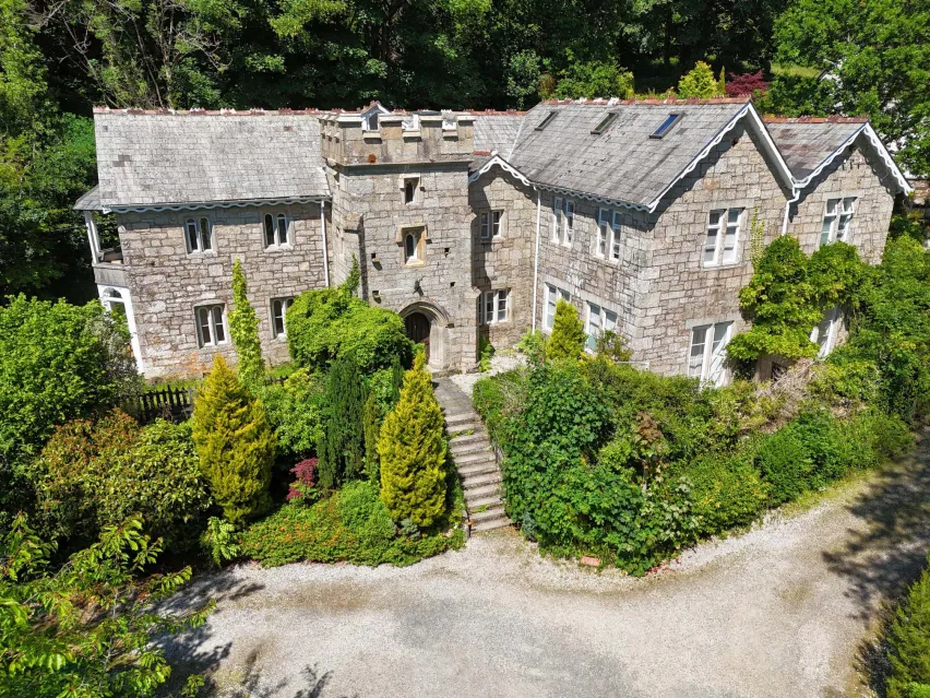 Large stone built detached property surrounded by green trees and. bushes