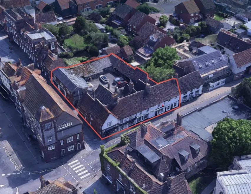 An aerial view of Baldock market town comprising a number of buildings and a main road with zebra crossing. The property for auction is highlighted with a red outline. 
