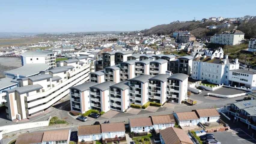 An aerial shot of mulitple, multi storey, white painted apartments surrounded by several bungalows and houses with blue sky in the background
