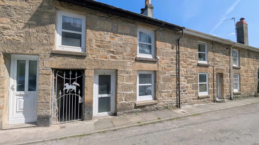 Row of pale brown brick, two storey terraced houses with white frames windows. The sky is blue. 