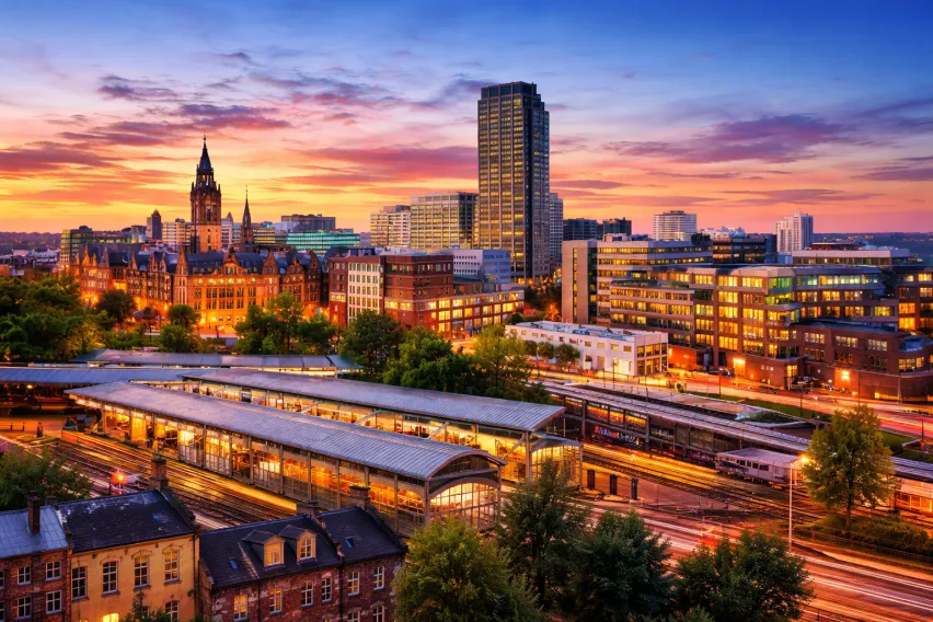 A multicolured sunset skyline of sheffield featuring the train station and different height buildings in the background. The colours are blue, purple, orange, yellow, pink and red mainly.