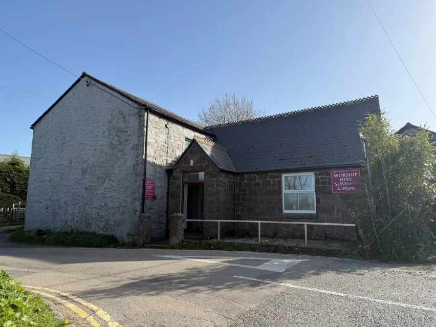Detached former church building on roadside location with blue sky behind