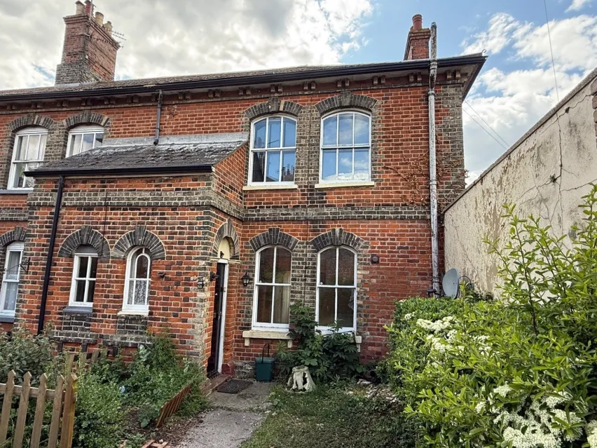 A brown brick period property with white framed windows on ground and first floor. Blue and white cloudy sky above.