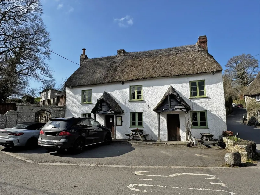Detached white building with thatched roof with two cars parked outsde and sitting next to a road.