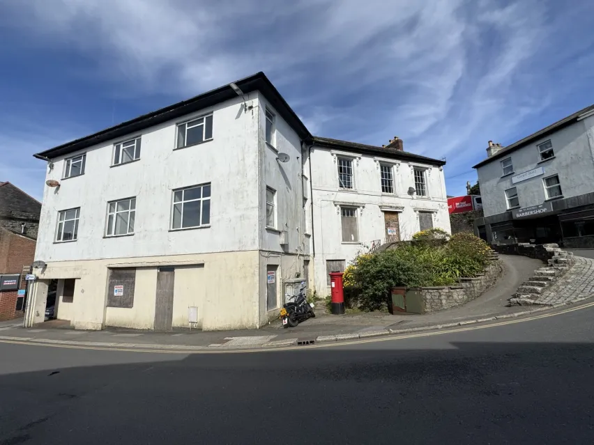 A large white building with three storeys sitting by the side of the road with blue sky above. 