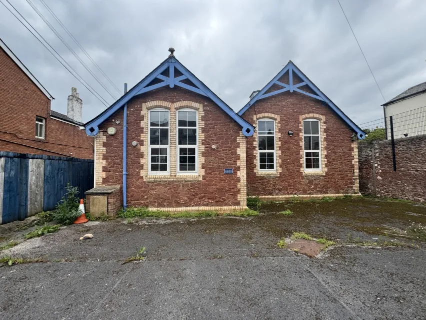 brown brick single storey building under pitched roof sitting on a tarmac hardstanding