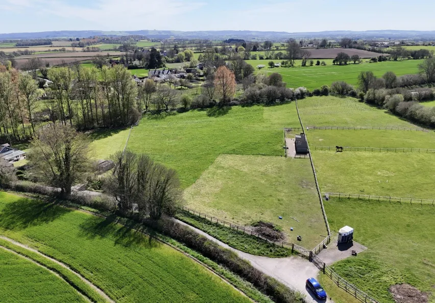Green fields and pasture land surrounded by trees with a country road through the middle.