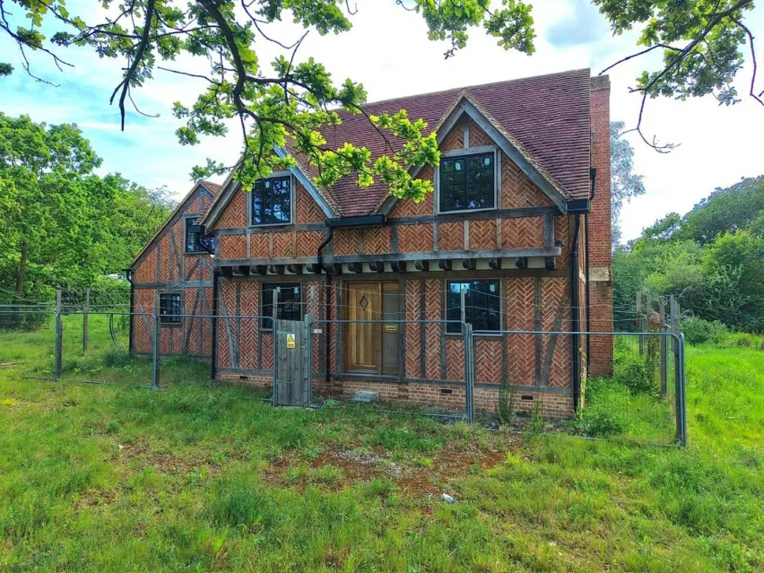 A detached brown brick tudor style house surrounded by green grass and trees