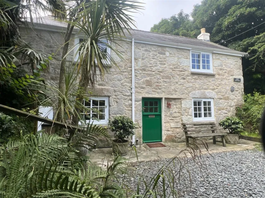 A pale stone house with green front door and brown bench outside the front, There are green palm trees in the foreground. For auction with Clive Emson Auctioneers on 17th June.