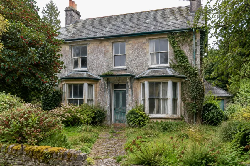 Weathered two-storey period house with an overgrown garden and neglected exterior.