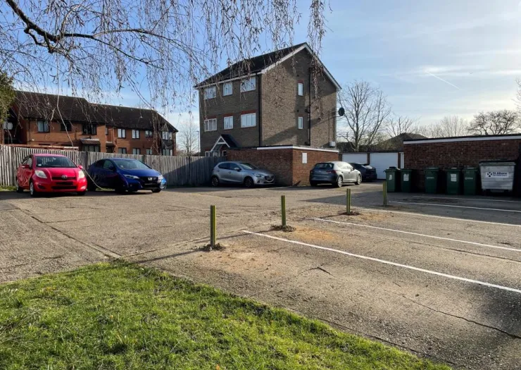 Apartment building parking lot with cars, bins, and grassy area.