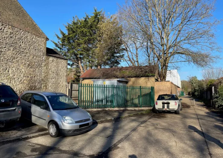 Cars parked near a fenced electrical substation and a stone building.