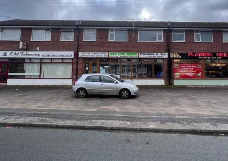 Brick building with takeaway shops, including K.W.Takeaway, White Cliffs Windows, and Flaming Grill. A silver car is parked i