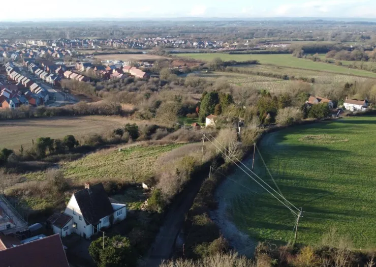 Aerial view of a rural landscape with houses, fields, and a new housing development in the distance.
