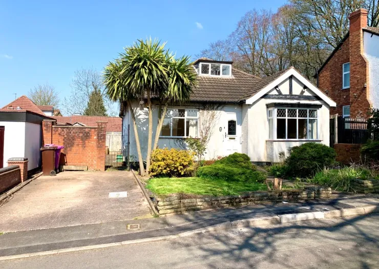 White detached bungalow with driveway, front garden, and palm trees.