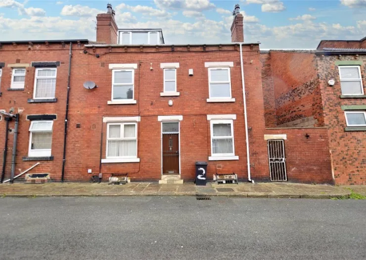 Red brick terraced house with white-framed windows and a brown door, viewed from across the street.