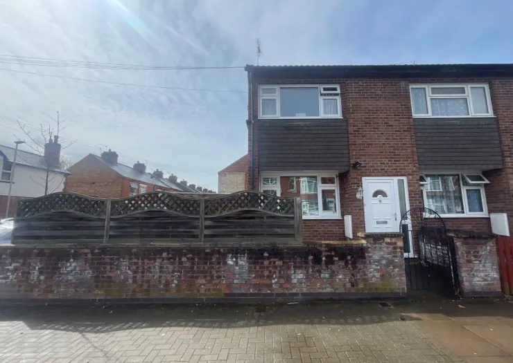 Red brick terraced house with white door, decorative fence, and brick wall.