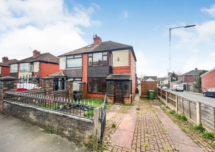 Red brick semi-detached house with driveway, front garden, and decorative metal fence.