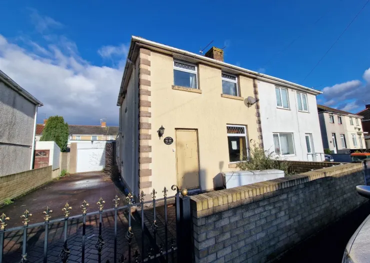 Cream-colored terraced house exterior with driveway, decorative gate, and brick wall under a blue sky.