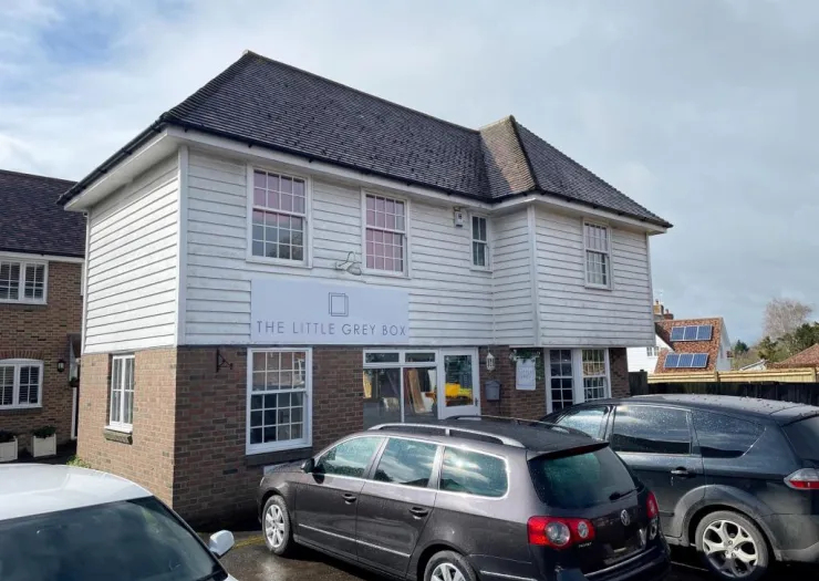 The Little Grey Box" building exterior with white clapboard siding and parked cars.