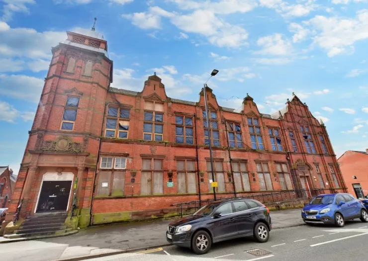 Large red brick building with boarded-up windows and a small tower under a blue sky.