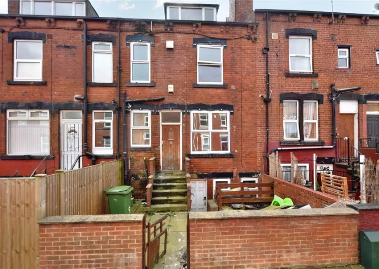 Red brick terraced house exterior with small fenced yard and steps leading to back door.