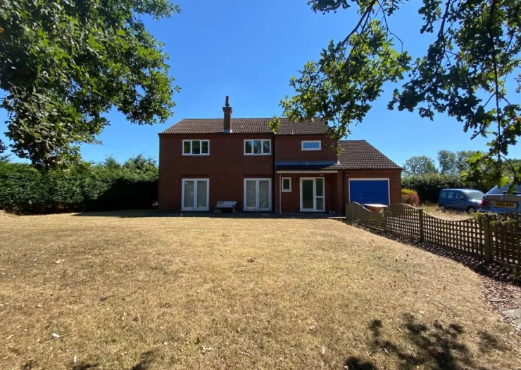Red brick two-story house with dry front lawn and trees on a sunny day.