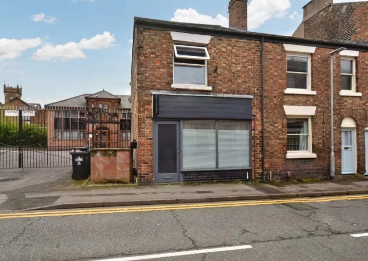 Brick storefront with gray awning and blinds, next to a gated building.