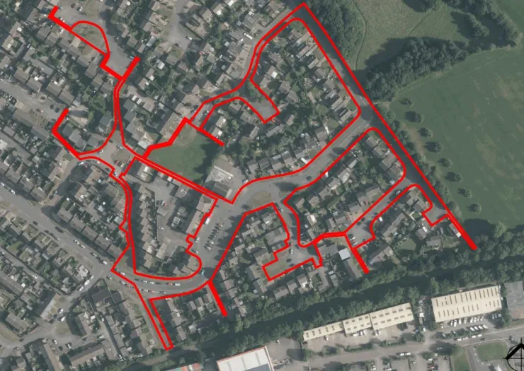 Aerial view of a residential area outlined in red, showing houses, roads, and green spaces.