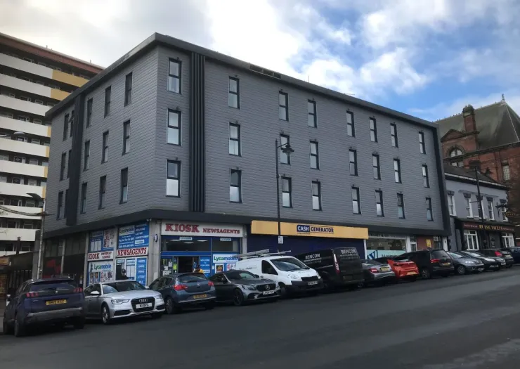 Modern gray mixed-use building with "Kiosk Newsagents" and "Cash Generator" shops on ground floor.
