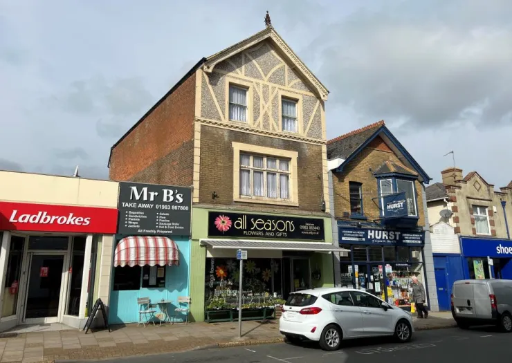 Storefront view of "All Seasons" florists between a takeaway shop and "Hurst" store.