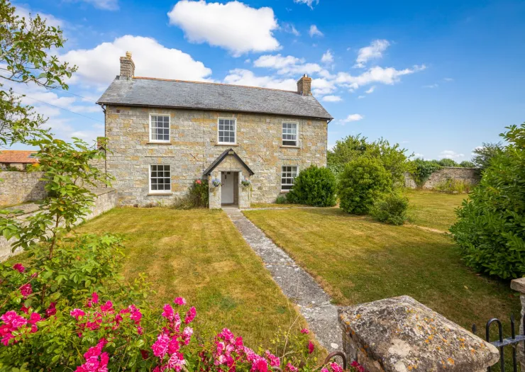 Charming stone farmhouse with front garden, pathway, and vibrant pink roses.
