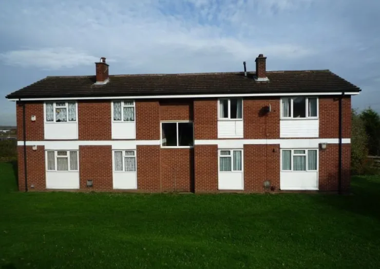 Red brick apartment building exterior with white trim and green lawn.
