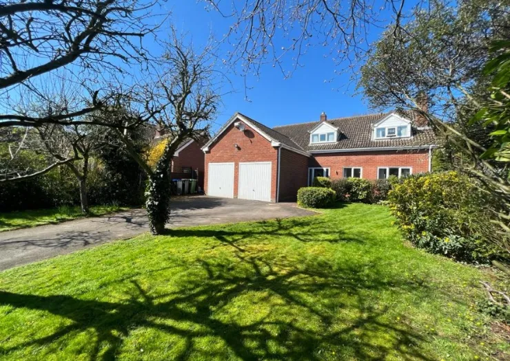 Red brick house with double garage and green lawn on a sunny day.