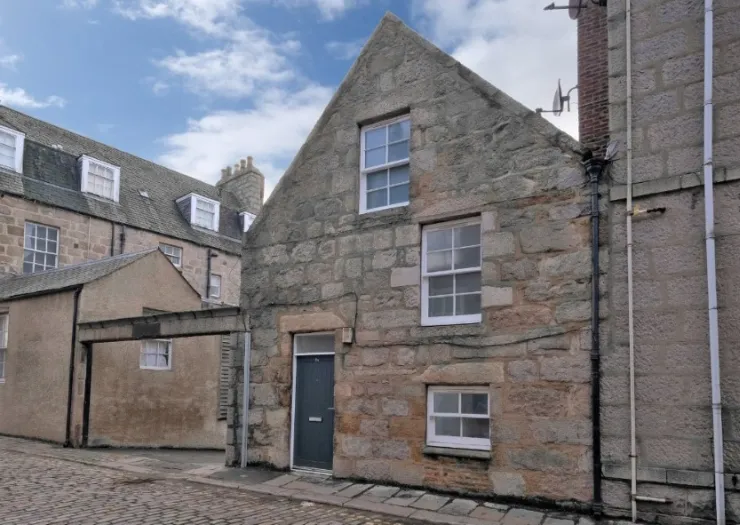Stone house exterior with white-framed windows and a gray front door on a cobblestone street.