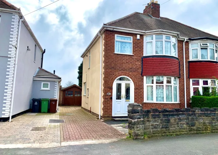 Red brick house with bay windows, white front door, driveway, and small front garden.