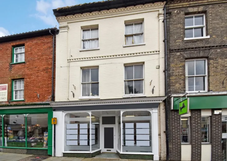 White storefront with blank window displays between other shops on a town high street.