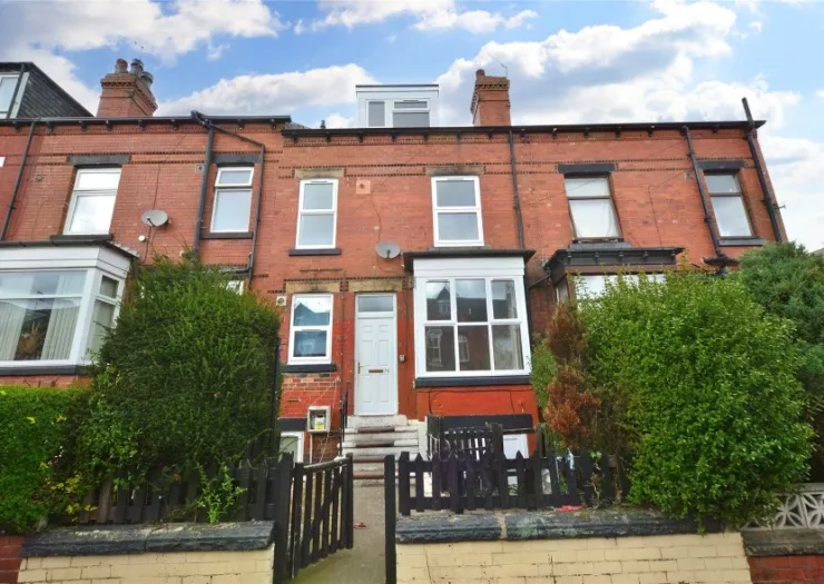 Red brick terraced house with white bay window, open gate, and steps leading to the front door.