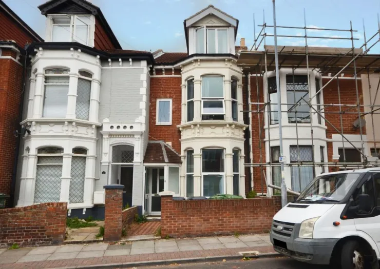 Victorian terraced houses, one with scaffolding, under partly cloudy sky.