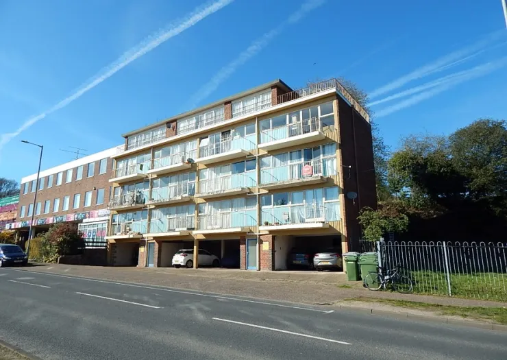 Coastal apartment building with balconies, under-building parking, and adjacent street.