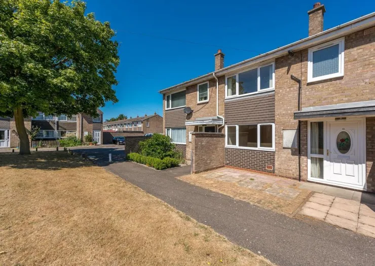 Attached house exterior with brown brick, white door, and small paved front yard on a sunny day.