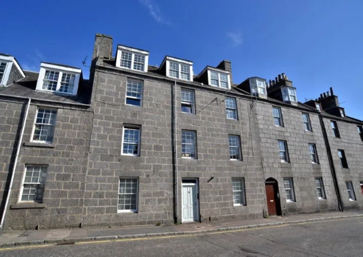 Grey stone apartment building with white-framed windows under a bright blue sky.