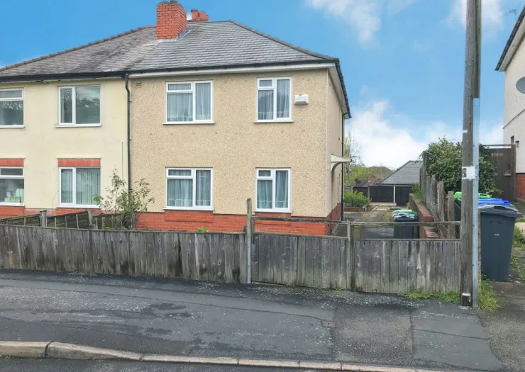 Semi-detached house with cream exterior, white windows, and wooden fence, viewed from street.