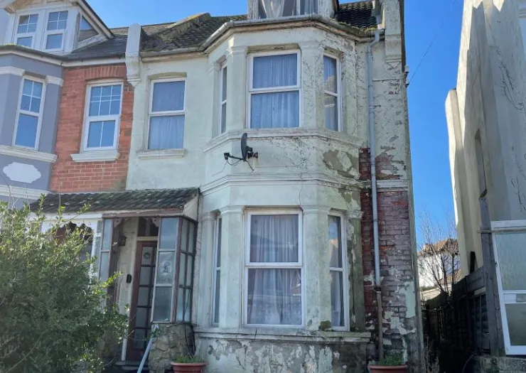 Semi-detached house with peeling paint, bay window, and small porch. Needs renovation.