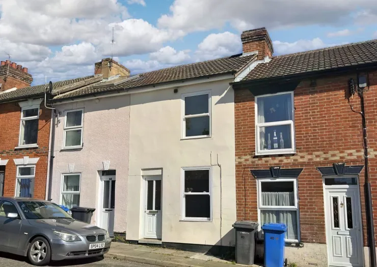 Row of terraced houses with brick and painted facades, white windows, and chimneys under a blue sky.